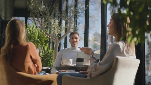 Three friends in a restaurant talking smiling and drinking tea. Business colleagues having a meeting after work or during coffee break at a cafe bar..