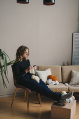Vertical full length portrait of calm woman knitting while enjoying cozy weekend at home. Crafting and handmade. Lifestyle and beautiful natural contour light.