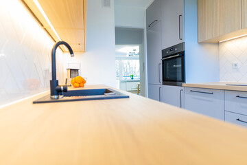 A modern kitchen with a bright worktop and white cabinets. View of a large room. Kitchen equipment, black sink and oven.