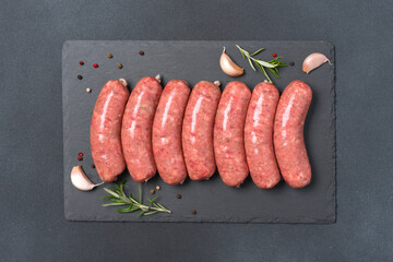 Raw bratwurst or pork sausages with seasonings on slate plate over black stone background with copy...
