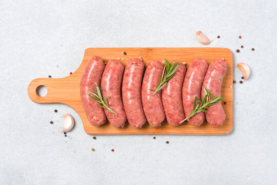 Raw sausages or bratwurst with seasonings on wooden cutting board over white stone table background. Traditional pork sausages ready to grill. Overhead viiew