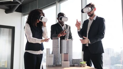 Multiethnic creative business team using virtual reality headsets at the meeting in modern office. Group of developers using virtual reality simulators, standing around table with 3d city model - Powered by Adobe