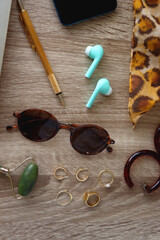 Book, tablet, phone, pen, glasses, wireless headphones, face roller, gold jewelry and leopard pattern scarf. Top view, wooden background.