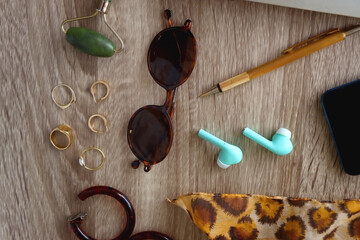 Fototapeta na wymiar Book, tablet, phone, pen, glasses, wireless headphones, face roller, gold jewelry and leopard pattern scarf. Top view, wooden background.