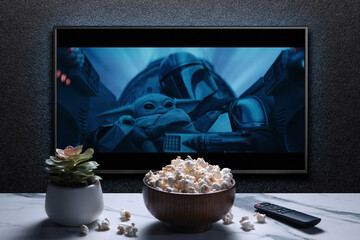 Naklejka premium TV screen playing Mandalorian trailer or movie. TV with remote control, popcorn bowl and home plant. Moscow, Russia - January 18, 2023.