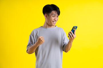 image of a handsome young man using his phone and posing on a yellow background