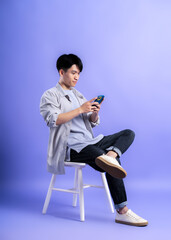 full body image of young asian man using phone on purple background