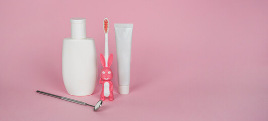 A set for children's oral hygiene: a toothbrush with a bunny, toothpaste, mouthwash and a dental mirror. The concept of dentistry and healthcare. Banner, pink background. Copy space for text