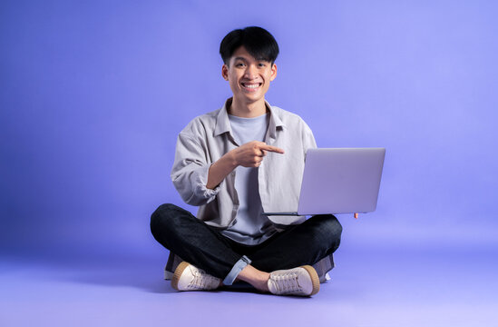 full body image of young asian man using laptop on purple background