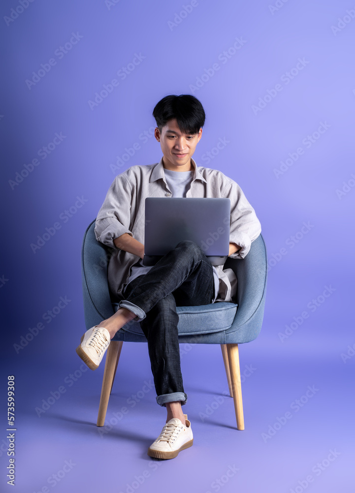 Wall mural full body image of young asian man using laptop on purple background