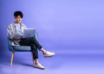 full body image of young asian man using laptop on purple background