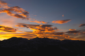 Dark orange landscape, mountains silhouette with a view of sunset sunbeams glowing behind the clouds