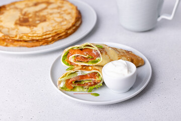 Pancakes with salmon (trout), sour cream and greenstuff. Thin, not sweet blinchiki stuffed with red fish. Traditional Russian and Ukrainian dish. Feast of Maslenitsa. Selective focus, close-up.