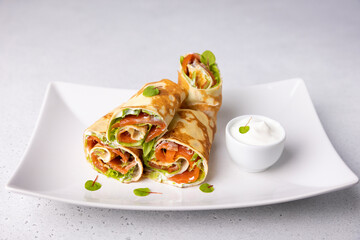 Pancakes with salmon (trout), sour cream and greenstuff. Thin, not sweet blinchiki stuffed with red fish. Traditional Russian and Ukrainian dish. Feast of Maslenitsa. Selective focus, close-up.