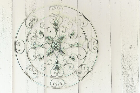 tinted green round metal ornate artwork against wooden wall 