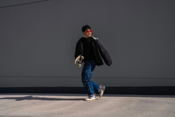 young asian man with cool red glasses running with skateboard in hand smiling urban lifestyle