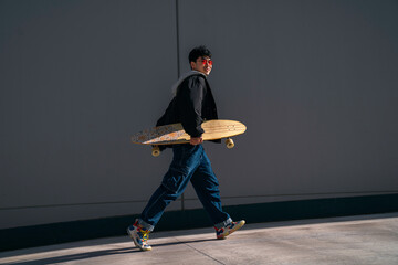 young asian man with red glasses walking happy with surf skate in hand urban lifestyle