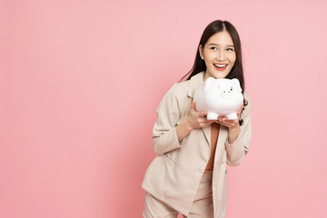 Happy Asian woman holding white piggy bank isolated on pink background, Saving money and financial...