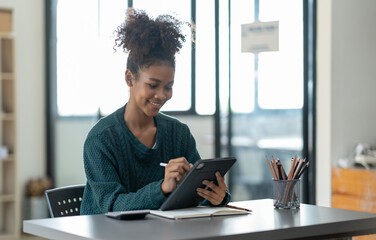 Attractive young african american businesswoman smiling thinking plan writing in a notebook and talking through tablet and laptop work from home looking at the camera at the office.