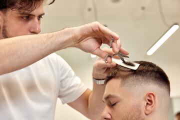 Obraz na płótnie Canvas hairdresser does haircut for caucasian bearded man