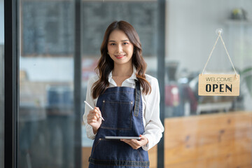 Asian female worker or barista standing smiling and holding the tablet in front of cafe working...