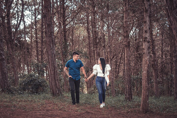 Pareja joven latina caminando tomados de la mano en un bosque de pinos