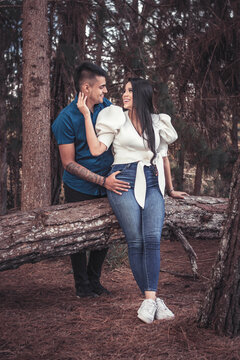 Pareja joven latina en un bosque de pinos abrazados mirandose con amor