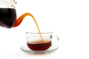 Fragrant black tea is poured from a teapot into a glass cup. White background.