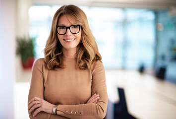 Attractive middle aged businesswoman standing with arms crossed at the office