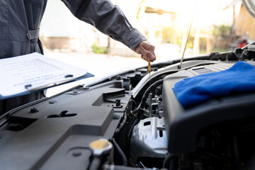 Maintenance engineer or auto mechanic pulls engine oil dipstick to inspect and check mileage of car, oil change ready to check information Enter record details in the car maintenance service file.