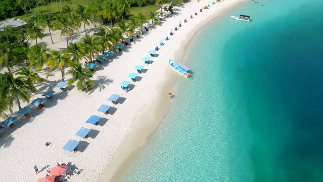 Aerial view of blue sun umbrellas row and chaise-lounges on the beautiful tropical beach with white sand and turquoise water. Excursion to the Morrocoy National Park, Venezuela