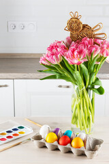 Easter eggs with paints, a wicker chicken and a bouquet of tulips on the table.