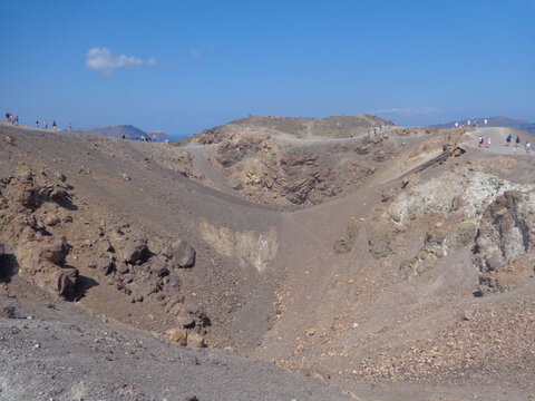 People visitng Santorini volcano crater with a blue sky day.