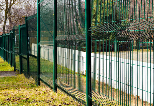 green painted metal wire fence between steel circular posts. transparent screen. welded wire mesh. green grass in the background. sport field beyond.