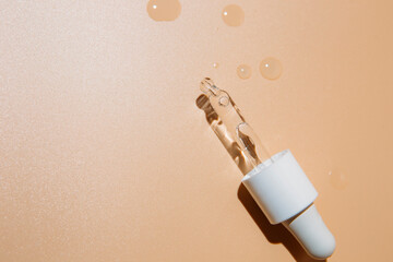 close up of pipette with pouring liquid serum and shadows on beige background. Trendy cosmetics shot with hard shadows.