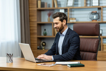 Obraz premium Successful mature businessman lawyer working inside classic modern office, modern man satisfied with work working with laptop at workplace, boss in business suit satisfied with achievement results.