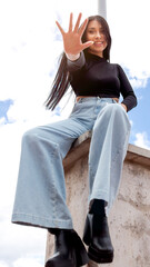 Young brunette woman with straight hair shows palm of hand wearing wide blue jeans and black blouse...