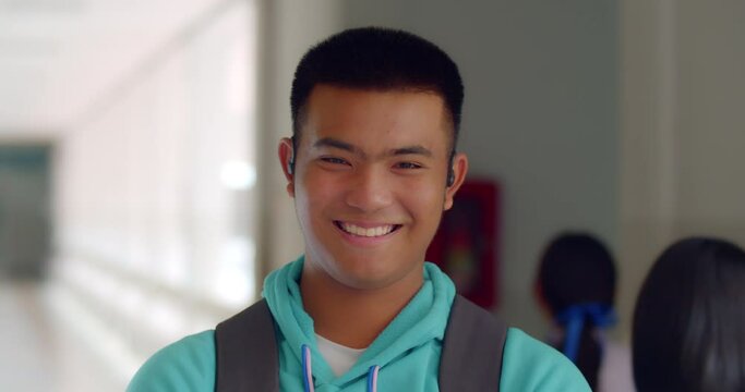 Slow motion scene of a happy smiling male high school student standing on a corridor in a school building with a laptop backpack.
