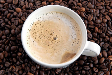 White Cup of Hot Coffee with Milk Foam on Coffee beans background. Cup of Hot Latte and Saucer....
