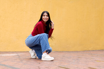 A Stylish and Relaxed Young Woman in a Bold Red Jacket and Blue Jeans on a Soft Yellow Background