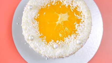 Cake with orange and coconut shavings spun on a pink background.