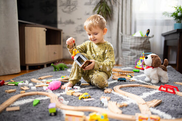 Baby playing with toy railroad, trains and cars on the floor