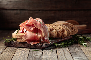 Prosciutto with bread and rosemary on an old wooden table.