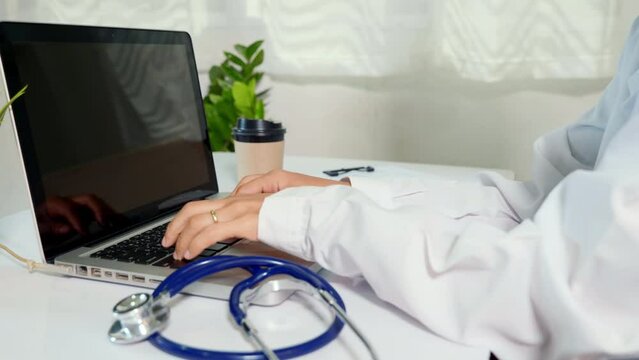 Doctor or nurse woman in uniform with stethoscope working she typing information of patient prescription from paperwork medical history form into laptop computer for record document data report