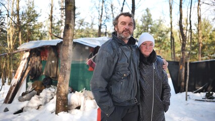 A homeless woman and a man pose in the woods in winter.