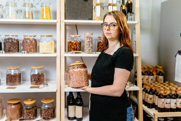 Female shop assistant work in organic grocery store. Young shopkeeper working in zero waste shop. Eco-friendly shopping at local small businesses.