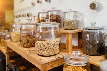 Big jar glass in a row. Zero waste shop interior. Wooden shelves with different food goods . Eco-friendly shopping at local small businesses.