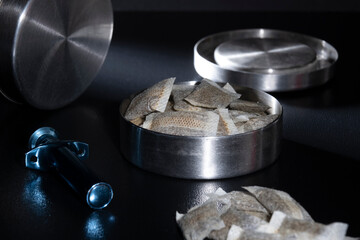 Closeup of a metallic Swedish snus can with white portion snus pouches. A blue loose snus portioner in the foreground