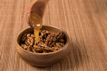 proper nutrition, honey is poured on walnuts in a wooden bowl from a wooden spoon