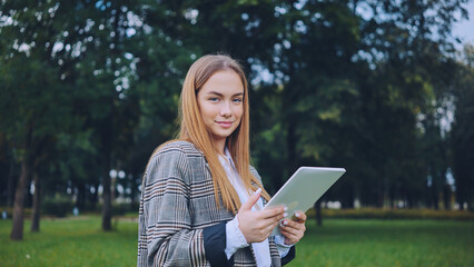 Fototapeta premium A young girl walks with a tablet in the park.